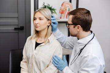 Otolaryngologist doctor checking young woman's ear using otoscope or auriscope at ENT clinic. Hearing exam