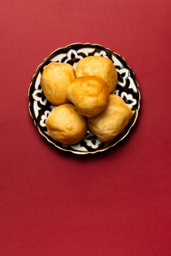 Kazakh baursaks on a traditional plate. Golden fried dough with a soft texture. Placed on a red background. Festive dish for Nauryz.