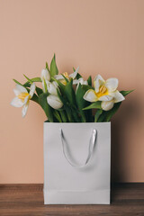 
A bouquet of beautiful white tulips in a gray paper bag without inscriptions on a light background.