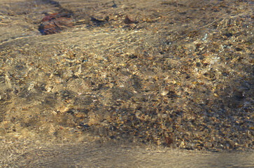 Water ripples in stream with light reflecting on them and pebbles under water