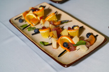 Fresh fruit skewers presented on a ceramic plate at a culinary event in a sunlit kitchen
