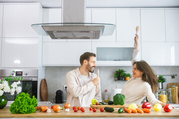 A joyous scene of a couple cooking in a modern kitchen full of fresh vegetables, reflecting an atmosphere of affection and teamwork.