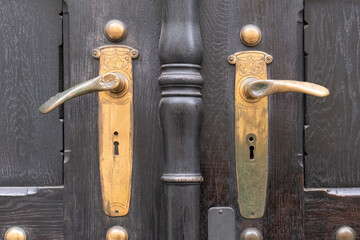 Antique European door handles made of aged brass with a gold-colored patina on a historic entrance, classic craftsmanship and elegance