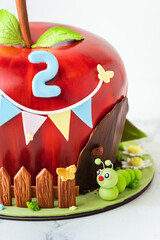 Red apple shaped fondant cake decorated with mastic edible caterpillar, green leaves and moss. Orchard fruits themed birthday cake isolated on white background