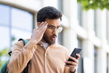 Upset student with phone in hand received notification with bad news, man with smartphone in hand...