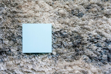A light blue sticky note on a textured rug. Ideal for office or home settings, emphasizing...
