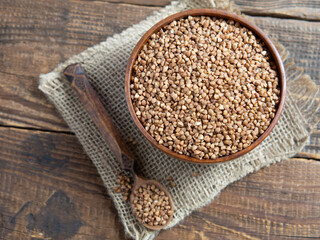 Organic buckwheat groats in a wooden bowl with a spoon on a linen napkin on a wooden table.
