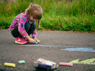 girl draws with colored chalk on the asphalt