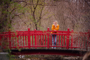 A thoughtful young woman stands on a vibrant red bridge, surrounded by the tranquility of autumn...