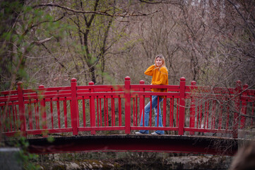A thoughtful young woman stands on a vibrant red bridge, surrounded by the tranquility of autumn...