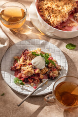 Apple crumble with ice cream on top decorated with mint leaves served in a plate on beige background in natural morning light