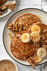 Healthy oatmeal pancakes with banana, nuts and honey on white tile background close up. Morning breakfast, top view. Pancake day or Maslenitsa recipe