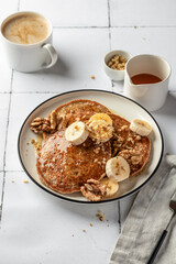 Healthy oatmeal pancakes with banana, nuts and honey on white tile background. Morning food breakfast concept. Pancake day or Maslenitsa recipe
