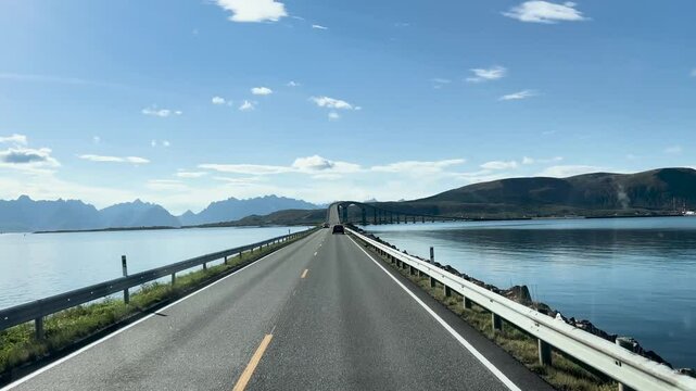 Vehicles are approaching a bridge on a scenic coastal road with mountains in Lofoten islands, Norway