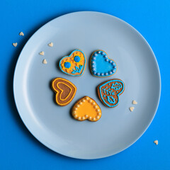 Cookies in shape of hearts decorated by yellow and blue icing and sprinkles on blue plate  against blue background