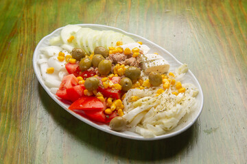 Tuna salad with various fresh ingredients served on white plate on green wooden table