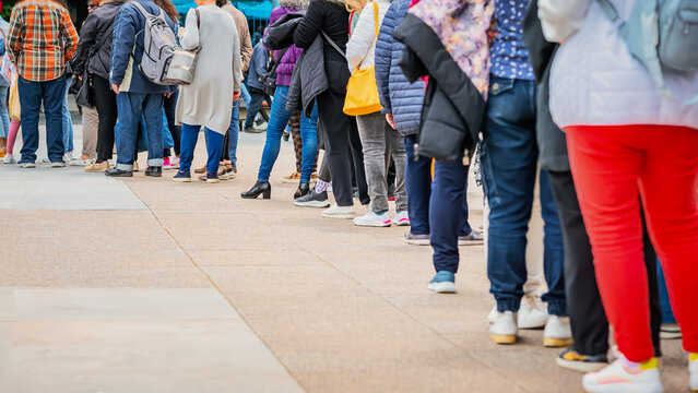 People standing in a long queue outdoors on city street. Public crowd. Women and men stand behind each other. Consumerism, waiting concept