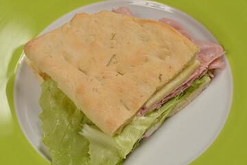 A sandwich with ham, cheese, and lettuce is displayed on a green plate, with a focus on the fresh ingredients and appetizing presentation
