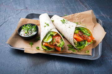 Italian style wrap piada tortilla with cured graved salmon, salad and avocado served as close-up with sour cream dressing dip on a tray