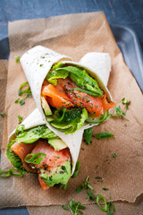 Italian style wrap piada tortilla with cured graved salmon, salad and avocado served as close-up with sour cream dressing dip on a tray