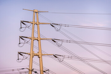 High voltage transmission lines take a turn at a tower at dusk
