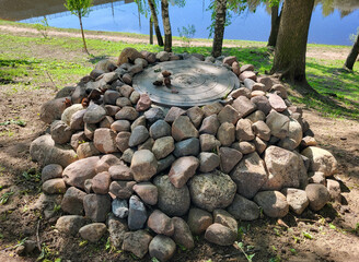 Above the river, a cast-iron hatch is decorated with cobblestones, and fallen fir cones are on the hatch cover.