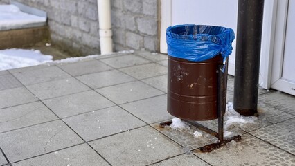 Obraz premium A brown dumpster with a blue trash bag is installed on the sidewalk next to the store. Close-up