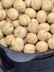 Large whole walnuts in large quantities in a black pot on the market for sale. Healthy eating. Close-up