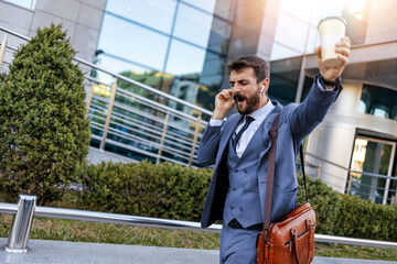 Excited Businessman Holding Coffee And Talking On Phone Outdoors
