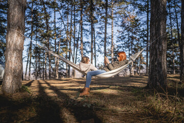 caucasian mother and her daughter small toddler girl in the hammock in nature in winter or spring...