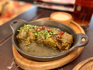 Delicious dolma (sarma) stuffed with grape leaf rice, with white yogurt sauce and pomegranate seeds. Lebanese dolma sarma on a wooden plate. Lebanese, Turkish, Greek, Middle Eastern cuisine. Close-up