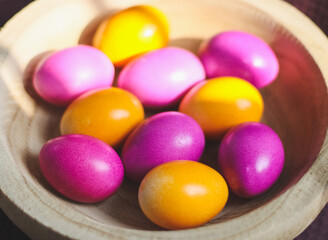 Colorful Easter eggs in a wooden plate on a dark burgundy kitchen towel.