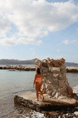 A woman in a floral swimsuit enjoys the beautiful view from a stone pier in the Mediterranean.