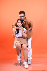 couple adult happy expression where man standing and woman sitting arms around holding hands on white chair very romantic ,couple wedding concept. isolated on orange background.