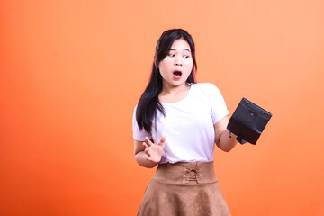 Naklejka premium A woman with a shocked face holding an empty wallet in front of an orange background