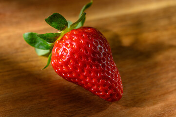 Fresh ripe strawberry resting on a wooden surface in soft natural light