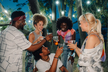 Friends toasting drinks at summer music festival under string lights