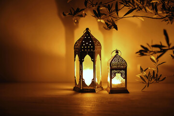 Two Moroccan lanterns on table at nigh. Blurred olive tree branches. Golden glow. Festive banner, invitation for Muslim holiday Ramadan Kareem. Eid mubarak celebration. Religion concept, copy space. © tabitazn