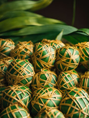 A close-up of beautifully woven ketupat, traditional Indonesian rice cakes wrapped in intricate palm leaves. The golden-yellow and green hues create a festive and cultural aesthetic.