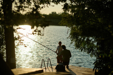 Father and son fishing together on wooden dock at sunset