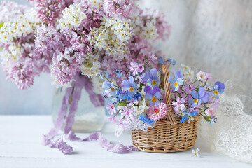 Spring still life with flowers, a bouquet of blooming lilacs and bird cherry in a vase, a basket with pansies, forget-me-nots and phlox, blur, beautiful card.