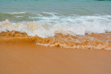 Ocean wave rolling over bright orange sand at the shoreline, creating contrast between water and beach.