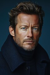 Obraz premium Captivating close-up of a man with striking blue eyes and tousled hair in a dark coat against a muted background