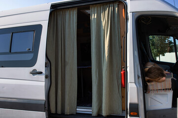 Side view of a camper van with open doors,  beige curtains and a resting traveler, capturing a cozy...