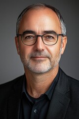 Obraz premium Mature man with glasses and beard poses confidently in a well-lit, neutral background during a professional photoshoot