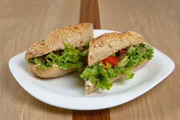 Delicious sandwich on a white plate filled with fresh lettuce peppers and other colorful vegetables