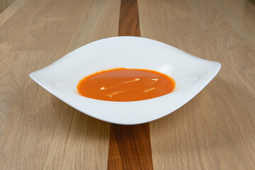 A vibrant bowl of homemade tomato soup garnished with swirls of cream presented on a light wood surface
