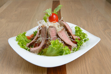 Gourmet steak salad with fresh lettuce tomatoes and a flavorful dressing on a white plate Delicious!
