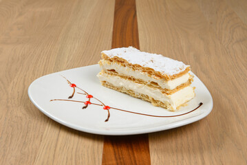 Creamy puff pastry delight: layers of flaky crust and sweet cream dusted with powdered sugar and chocolate sauce