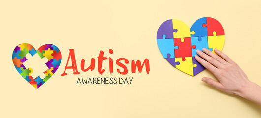 Female hand and heart made of color puzzle on yellow background. Concept of autistic disorder